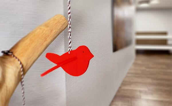 ein roter Vogel aus Filz hängt an einem Ast im Praxiseingang